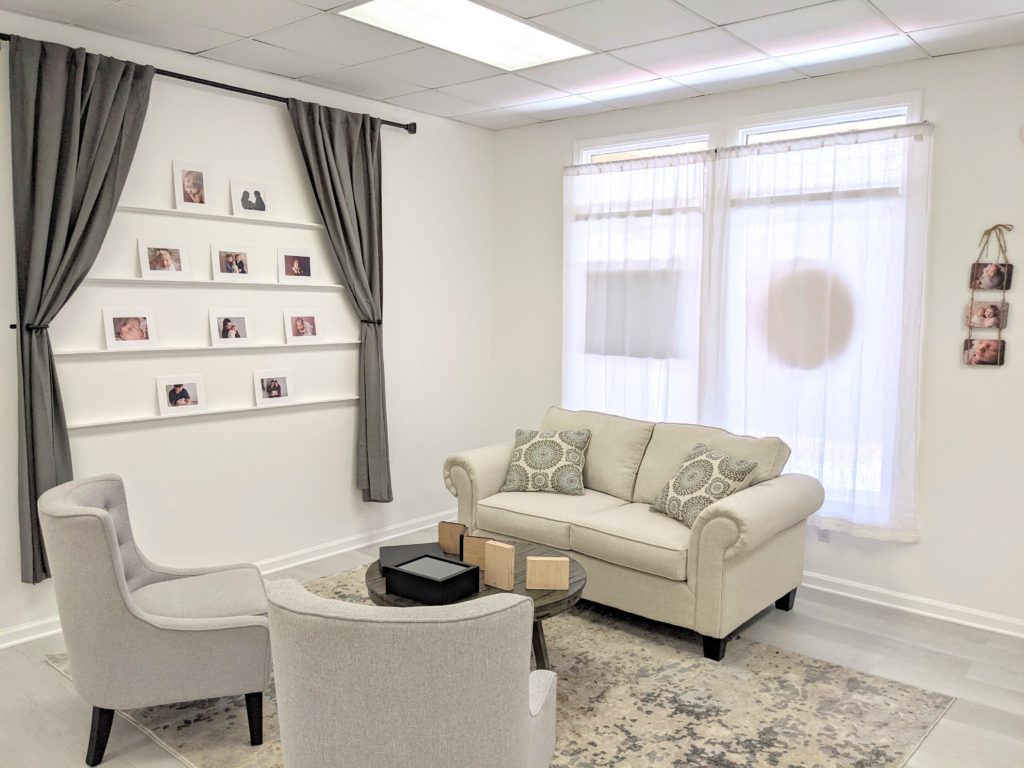 Photography studio sitting area with pictures of a newborn session displayed on a wall.