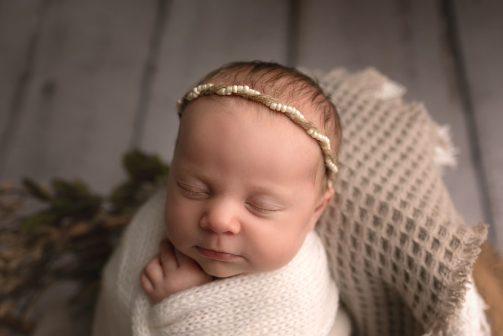 Newborn baby girl swaddled in cream wrap and white beaded headband.