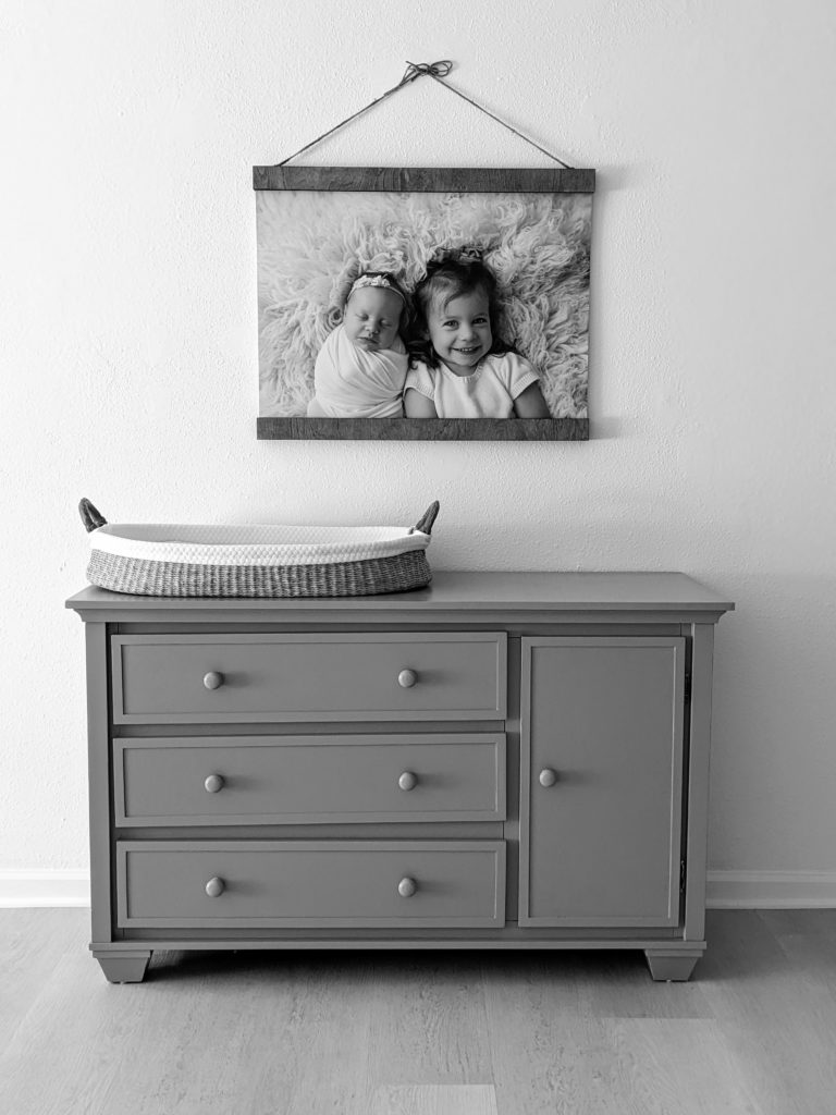 Image of changing table with hanging canvas above displaying newborn baby girl and older sister