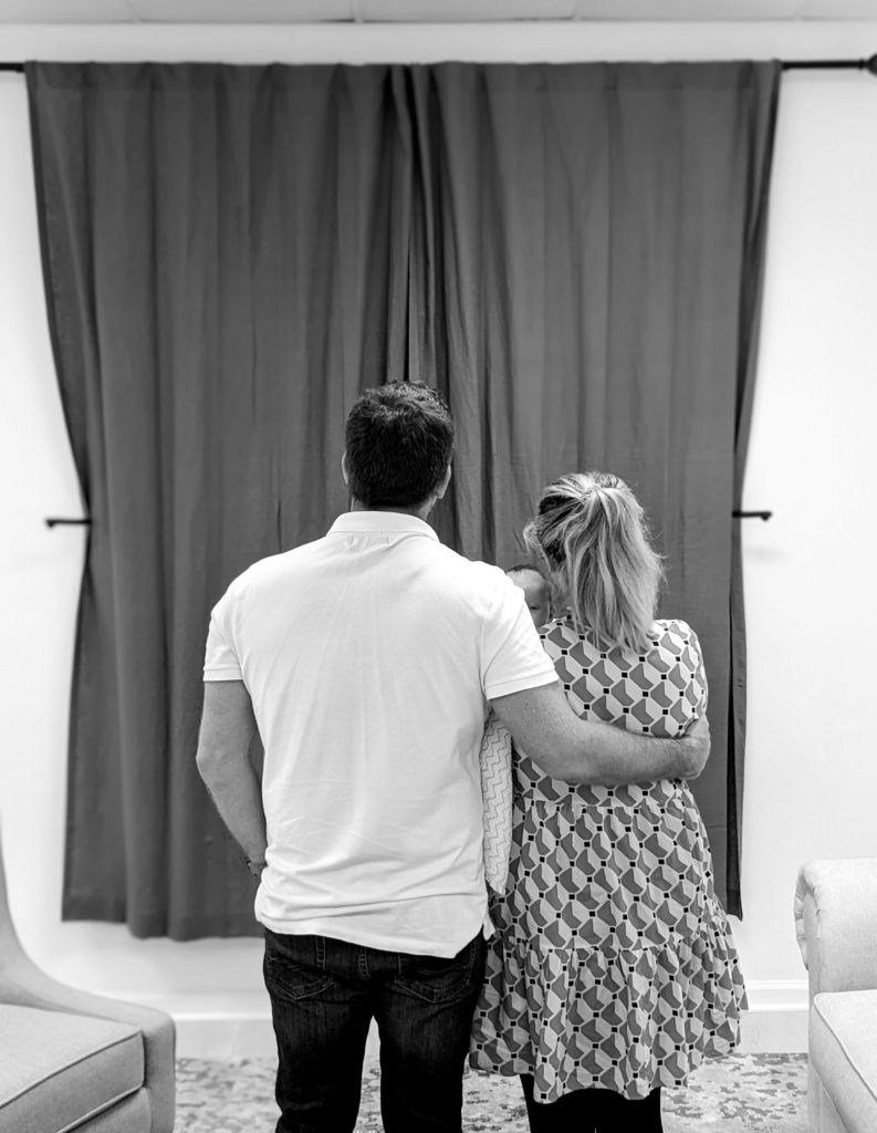 Newborn clients standing in front of reveal wall with curtain covering their images.