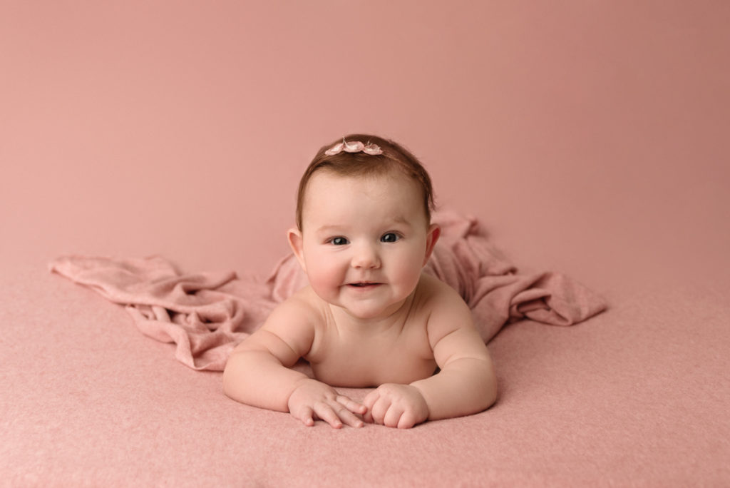 Baby girl laying on a pink blanket doing tummy time, smiling at the camera