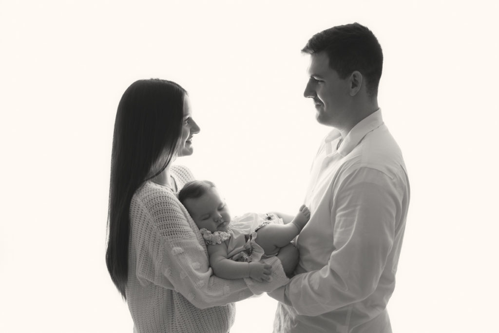Backlit profile image of parents holding their sleeping 6 month old daughter.