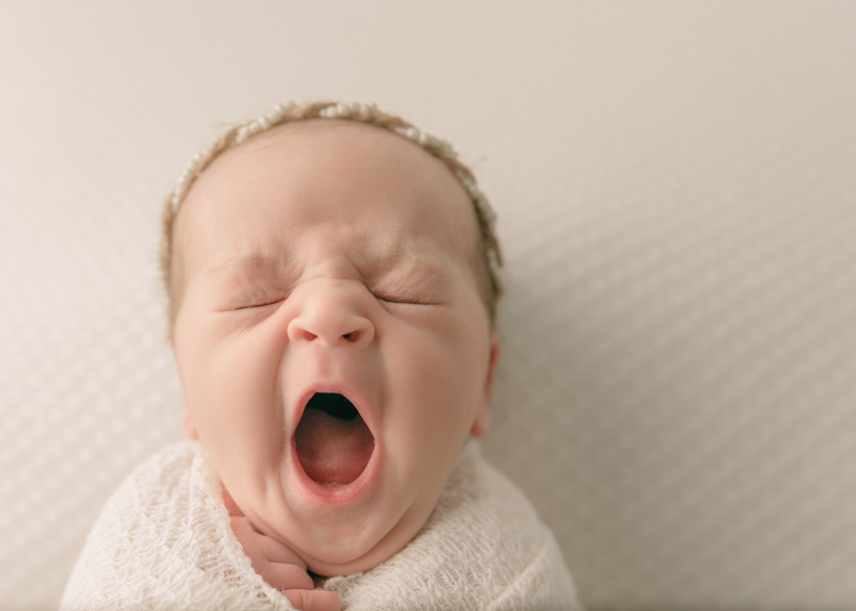 Newborn baby swaddled in cream blanket, yawning