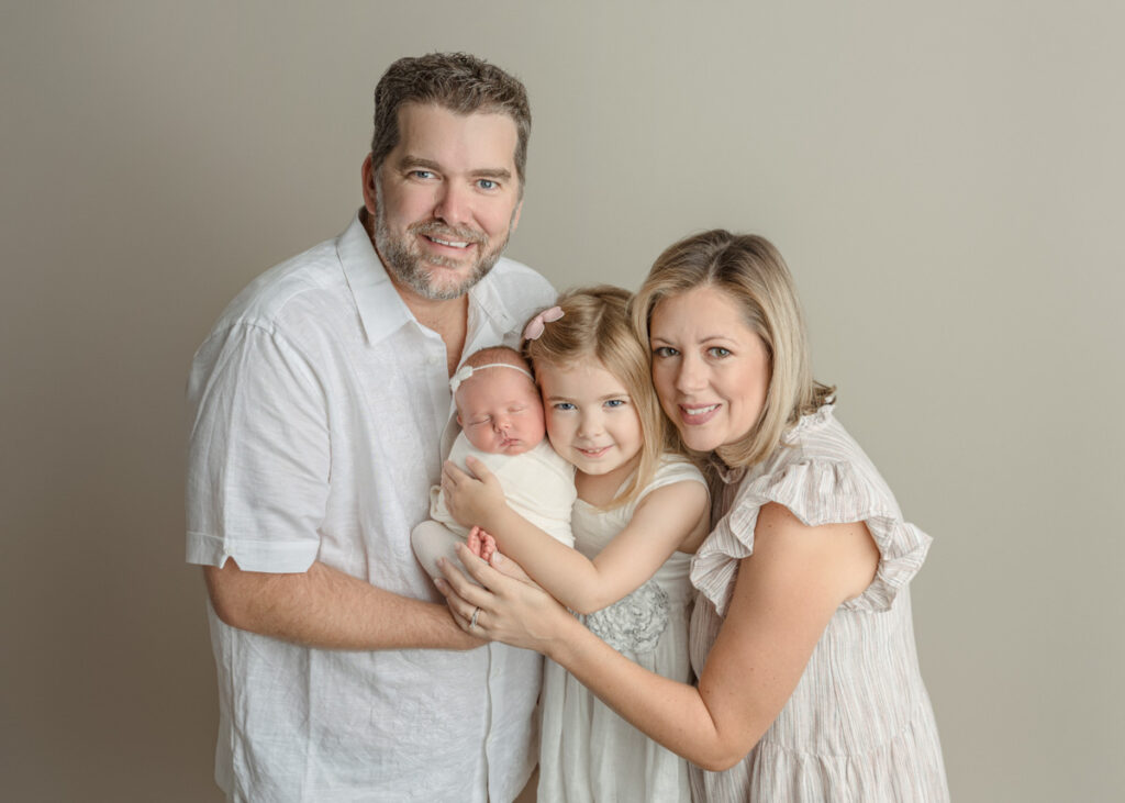 Family of 4 smiling cuddled together holding newborn baby girl