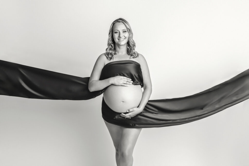 Black and white of expecting mom with black satin fabric draped across chest and below tummy.