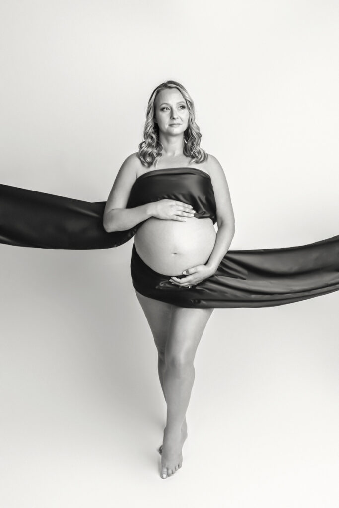 Black and white of expecting mom with black satin fabric draped across chest and below tummy.