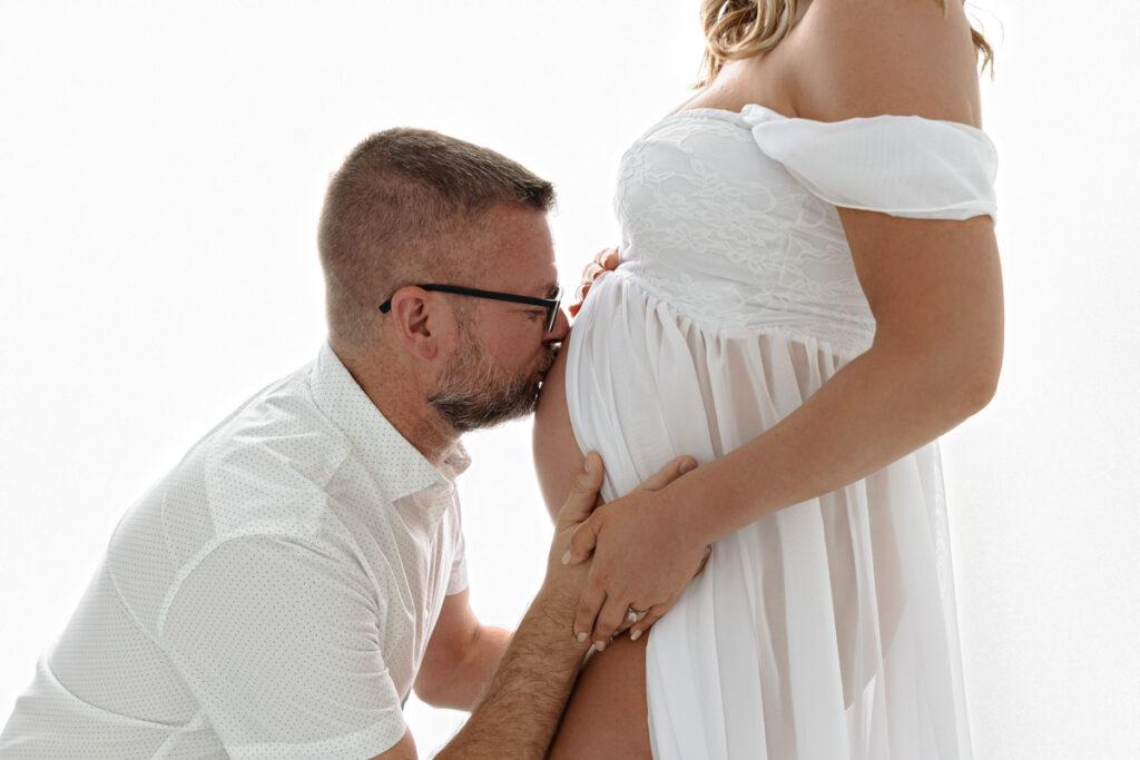 Backlit image of Dad kneeling and kissing expectant mom's belly