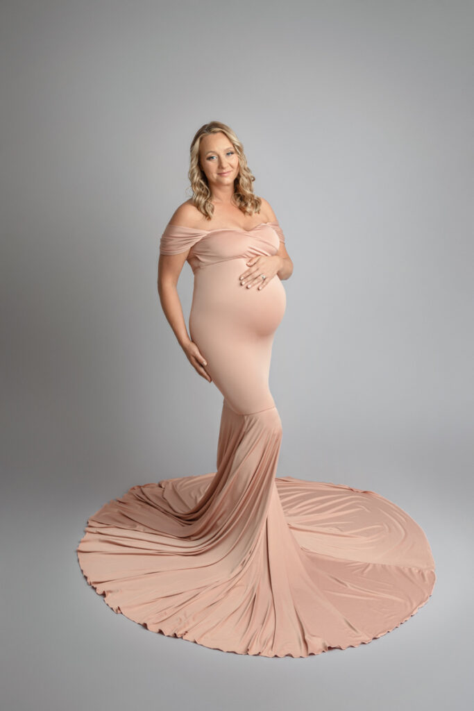 Expecting mother posing in a pink maternity dress on grey backdrop