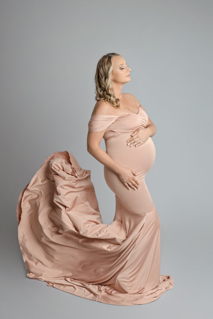 Expecting mother dressed in a pink flowing maternity dress with bottom of dress thrown up behind her.