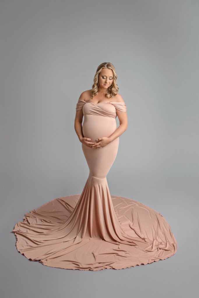 Expecting mom in pink long flowing dress holding belly underneath.
