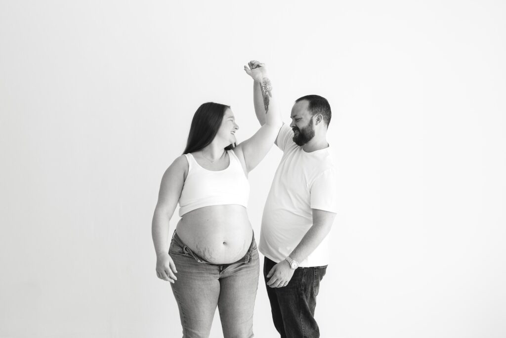 Black and white image of expecting parents twirling and dancing