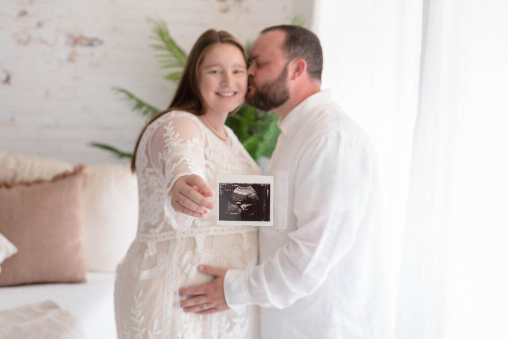 Expecting parents embracing while holding out a sonogram image of their unborn child.
