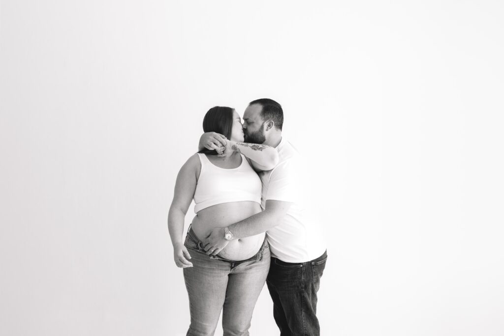 Black and white image of expecting parents embracing a kiss.