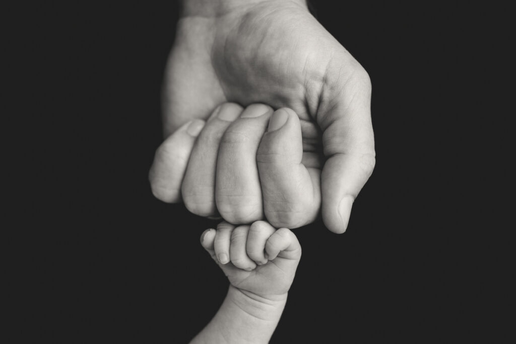 Close up black and white image of capturing dad fist bumping newborn baby's fist