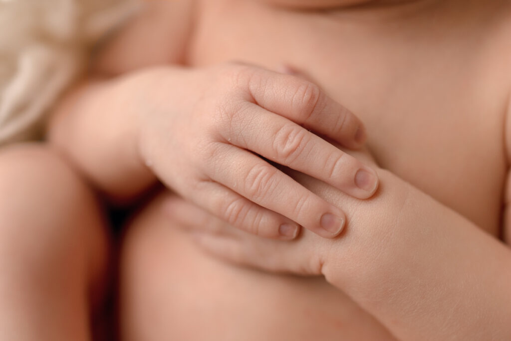 Close up image of capturing newborn baby's hands overlapping on her tummy.