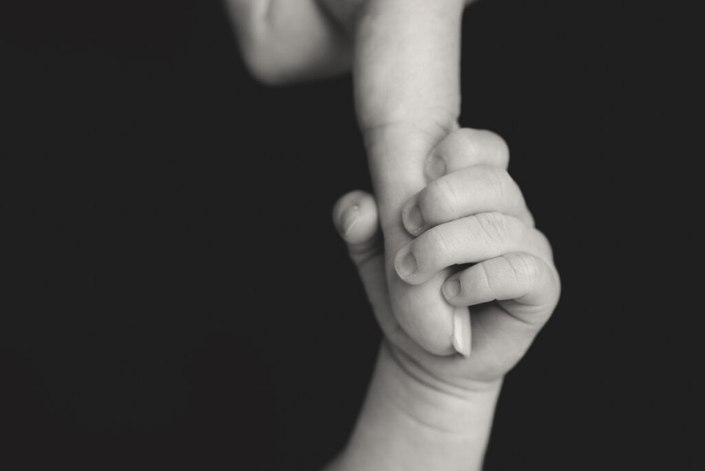 Close up black and white image of newborn baby holding Mom's pointer finger.