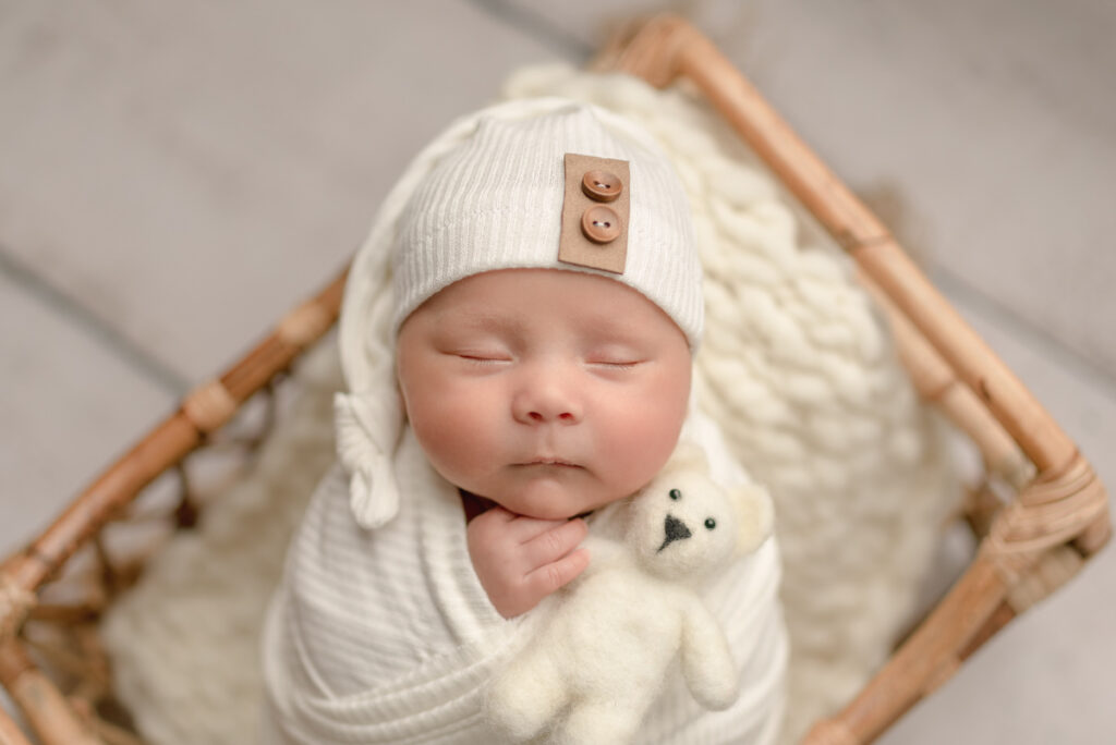 Gulf Breeze,FL Newborn Photographer baby boy swaddled in white, wearing a matching hat, and holding a teddy bear prop.