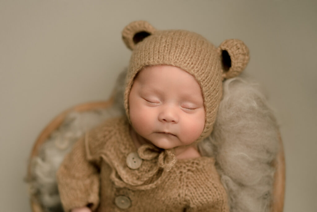 Pensacola FL Newborn Photographer Newborn baby dressed in a brown teddy bear outfit placed in a heart bowl prop.