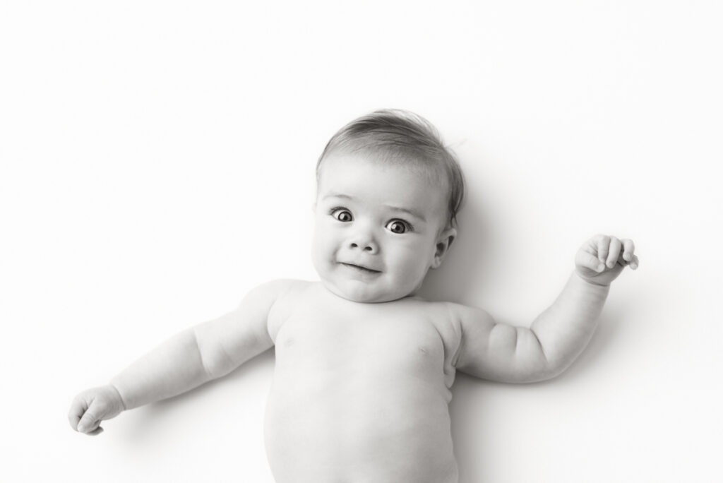 Black and white image of 4 month old baby laying on his back smiling at camera.