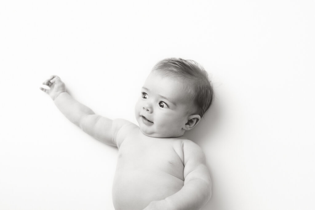 Black and white image of 4 month old baby laying on his back looking off to the side, and making a funny face.