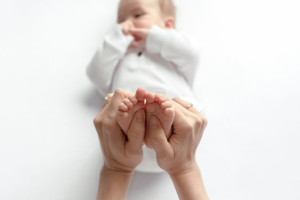 Close up image of a 4 month old baby laying on his back with his mom's hands holding his feet.