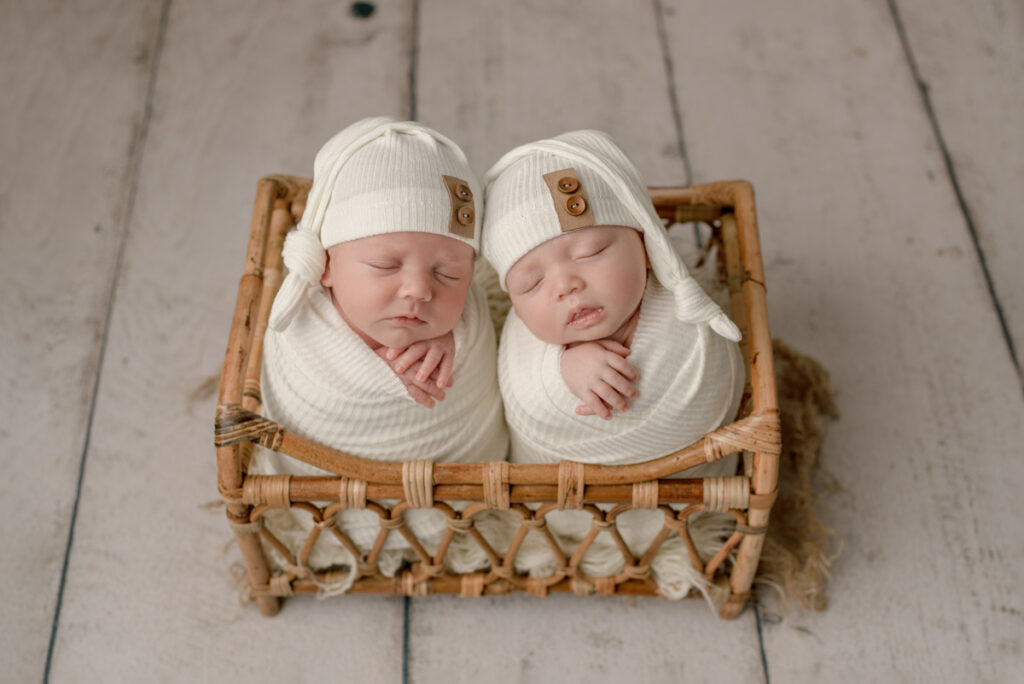 Navarre, FL newborn photographer twin babies in white swaddles and hats, placed in a wicker basket during a studio photography session.
