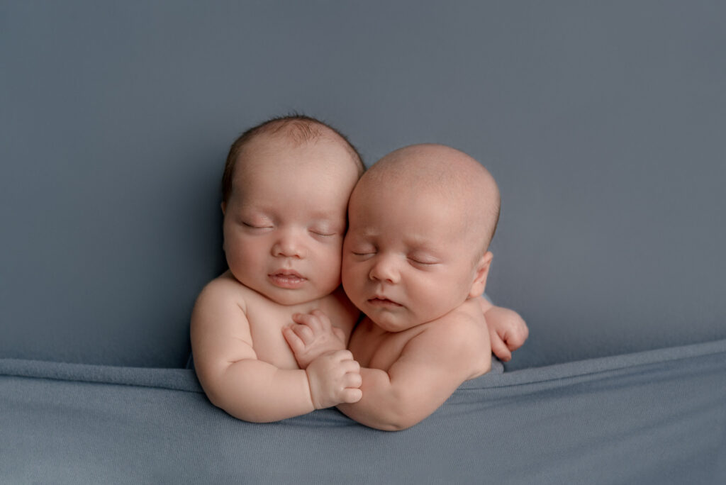 Pensacola, FL newborn photographer.  Baby boy twins snuggling together under a blue blanket during a posed studio session.